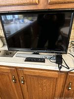Full view of Samsung 24-inch TV on a kitchen counter with remote and power adapter beside it.