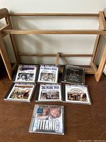 Seven original cast show tunes CDs and Titanic soundtrack laid out with a wooden CD rack standing behind them.