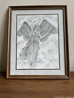 Full view of the framed black and white angel drawing depicting a female angel floating among clouds, signed and dated, in a wooden frame.