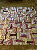 Full view of the vintage silk crazy quilt showing patchwork of multiple colored silk fabric squares and rectangles including pink, gold, burgundy, and pastel shades.