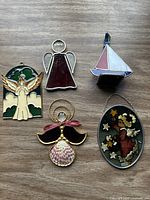 Five stained glass ornaments: four angels and one sailboat, displayed on a wooden surface in natural light.