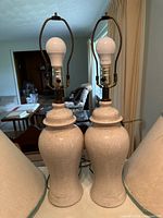 Pair of ceramic lamp bases without shades showing light beige speckled glaze and lamp hardware with bulbs.