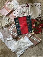 Top-down view showing assorted tablecloths, runners, and doilies in various fabrics, patterns, and colors including pink, white, red, green, and brown tones.