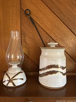 Photo showing both the pottery candle lantern with glass chimney and the pottery smudge pot with metal handle on wooden surface.