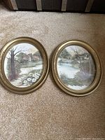 Pair of framed watercolor prints showing two scenic countryside estate scenes with streams and floral elements.