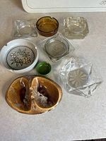 Photo showing eight vintage ashtrays with multiple shapes and materials including glass, ceramic, and pottery.