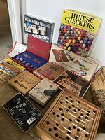 Photo showing multiple vintage board games and brain teasers including Rummikub, Chinese Checkers, Backgammon, Mill Game, and a wooden peg puzzle with game pieces and cards.