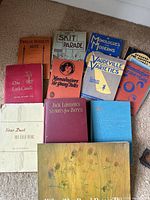 Top-down photo showing all twelve vintage books arranged together on a carpeted floor, titles visible including skits, monologues, and stories for young people.