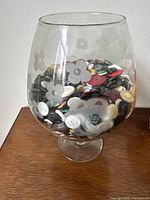 Clear oversized glass vase with frosted flower patterns filled with assorted vintage buttons
