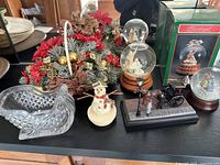 Photo showing the full assortment of Christmas decorations on the table including all snow globes, wreath, glass bowl, snowman, and horse carriage figurine.