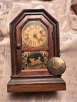 Front view of the vintage wooden pendulum clock with Roman numeral dial and decorative artwork on lower panel.