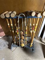 Full view of vintage croquet set including multiple wooden mallets with colored bands, balls, metal wickets, and wooden stand.