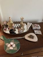 Display of vintage mirrored tray with various items including trinket dishes, figurines, hand mirrors, and Avon perfume bottles.