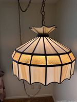 Side view of the vintage slag glass swag lamp lit up, showing the beige and amber glass panels and decorative scalloped edge.