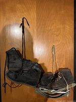Two pairs of vintage ice skates: one large black leather high-top pair and one smaller brown leather pair with metal blades and laces, hanging on a wooden wall.