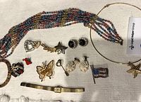 Full view of vintage mixed costume jewelry lot on cloth background including pins, brooches, earrings, necklaces, and wristwatch.