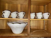 Milk glass punch bowl with 12 cups arranged on wooden shelving.
