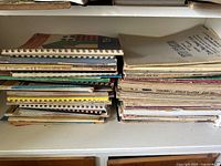 Stack of vintage organ sheet music books and loose sheets on a white shelf with some visible wear, broken bindings, and damaged pages