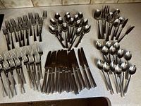 Full view of all flatware laid out on surface showing forks, spoons, knives, and serving pieces in matching design.