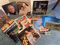 Photo showing a collection of vintage vinyl record albums featuring various artists such as Peter Paul & Mary, Dinah Shore, Perry Como, and others, with colorful illustrated and photographic album covers arranged on the floor.