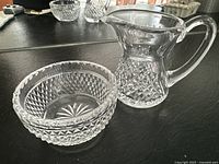 View of both Waterford crystal cream pitcher and sugar bowl together on a black surface.