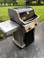 Side view of Weber Spirit gas grill showing folding side shelf, closed lower door, and black curved hood with thermometer.