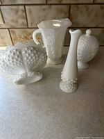 Photo of all four white hobnail and milk glass items including centerpiece bowl, bud vase, pitcher, and covered candy dish.