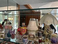 Shelf display showing Yankee Candle angel themed lantern with votive and tealight candles around it, glass taper holders, and various candle containers.