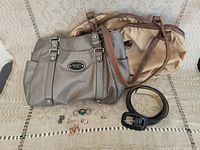 Group shot of two handbags, black belt, and assorted jewelry on a textured couch.