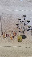 Photo showing the black metal candle holder with six arms and six glass votive candle holders decorated with multicolored leaf designs on each.