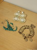 Photo of three costume jewellery items: white circular fringe earrings, turquoise bead bracelet, and silver-tone bracelet with dangling charms on wooden surface.