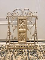 Full view of decorative wire shelf, showing curved top with metal leaves and wire sides with leaf motifs, and flat base for storage.