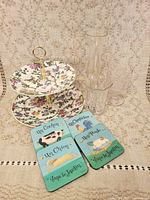 Two-tier floral dessert stand, two clear glass vases (one tall, one short), four animal-themed French coasters displayed on lace cloth