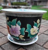 Front angled view of the ceramic flower pot and saucer showing colorful floral designs on a black background.