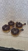 Four two-tone ceramic French onion soup crocks with lids and handles, light brown and beige, arranged on a cloth.