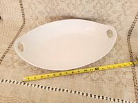 Top view of the white oval serving tray placed on a woven patterned textile background, showing tray shape and size.