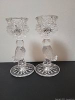 Front view of pair of glass lovebird candle holders showing bird detail and geometric patterned cup.