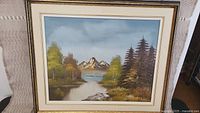 Full view of framed landscape oil painting showing river, trees, mountains, and sky.