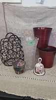 Photo showing all six items in the lot: black wire basket, clear textured glass vase, two red ceramic planters, small ceramic bell, and small silver-toned bowl.