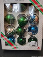 Full view of the set of 12 vintage glass Christmas ball ornaments in original packaging showing green, blue, and silver designs.