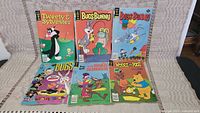 Photo showing six vintage comic books laid out on a beige fabric. Characters include Tweety & Sylvester, multiple Bugs Bunny covers, Wile E. Coyote, and Winnie the Pooh.