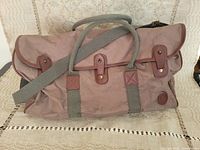 Full view of the vintage canvas duffel bag with leather handles, shoulder strap, and buckle closures.