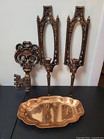 Full lot of vintage imitation brass decorative items including wall key, wall sconces, and tray on black surface against white wall.