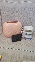 Photo showing a pink ceramic vase, three stacked soup mugs with colorful outdoor scenes, and pair of black owl salt and pepper shakers.