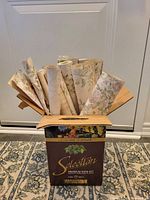 Rolled vintage wallpaper displaying floral and leaf patterns in a cardboard box