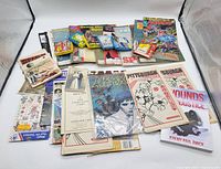 Wide layout view showing multiple Sports Illustrated magazines, Captain Armor comic, book titled 'Wounds of Justice', assorted postcards and smaller paper items.