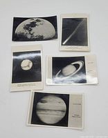 Front side of 5 planetary postcards showing images of Moon, comet, Saturn, Jupiter, and another planet in black and white photographic style.