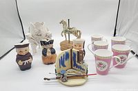 Full lot showing all items: cherub vase, Toby mugs, Hudson coffee cups, Goebel horse figurine, and small artistic brush set with palette.
