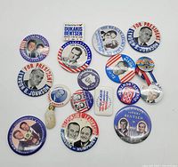 Photo showing a group of 15 vintage political campaign buttons laid flat on a white surface including Nixon, Johnson, Dukakis, Bentsen, Reagan, Humphrey and Gore themed buttons.