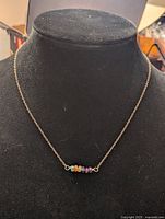 Front view of gold tone chain necklace with multi-colored beads centered on the display stand.